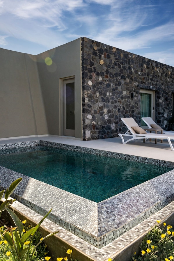 A modern outdoor pool area with a stone wall and two lounge chairs.