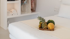 Une chambre à coucher avec un lit, une armoire où sont suspendus des vêtements, une étagère avec des serviettes pliées et un plateau de fruits.