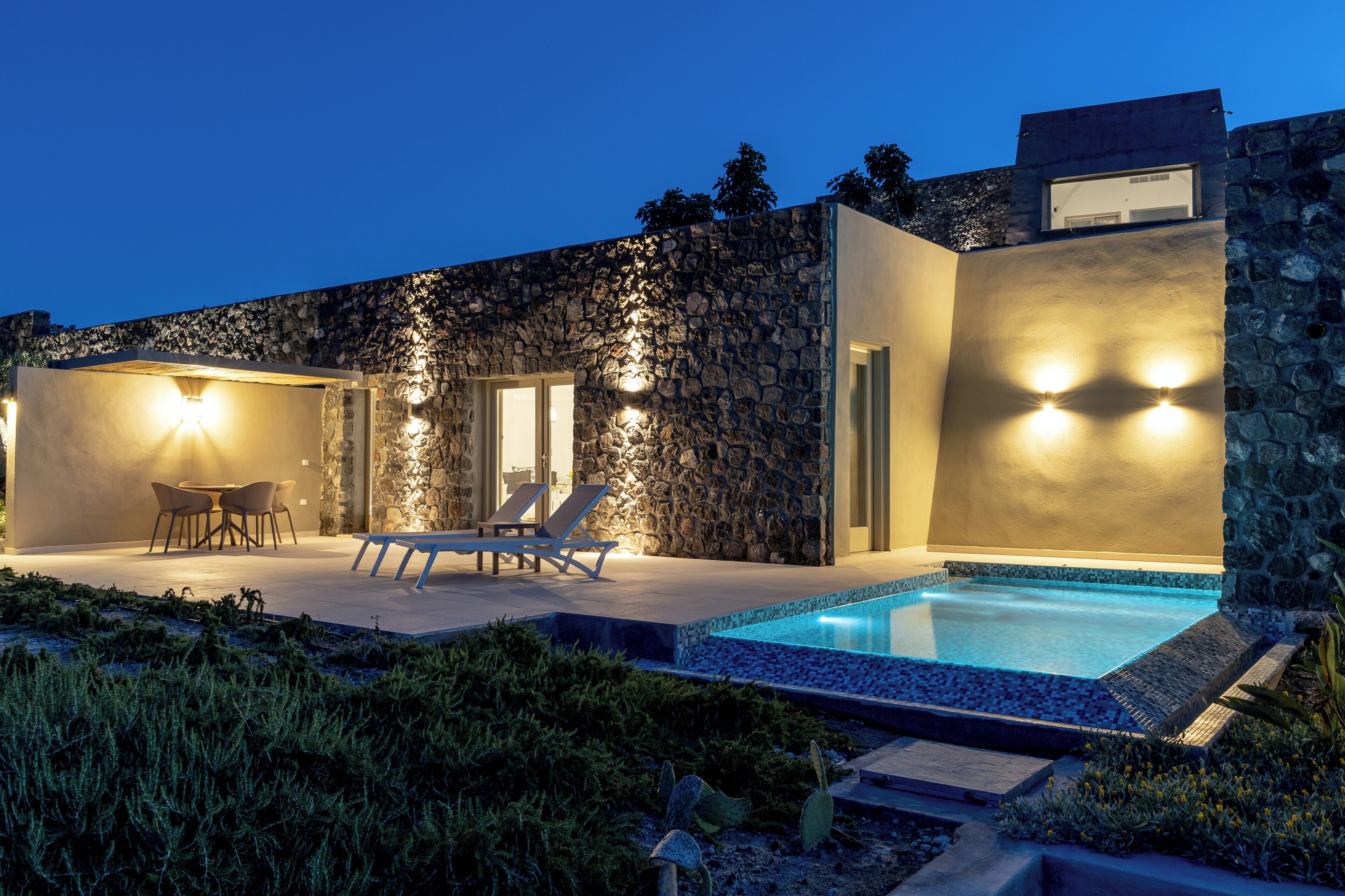 Une maison moderne avec une façade en pierre, une piscine et un espace salon extérieur.