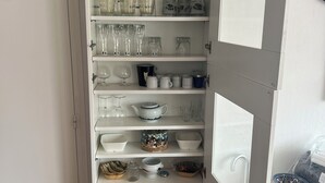 Keittiössä on valkoiset kaapit, joissa on erilaista lasiastioita, kulhoja ja pulloja.