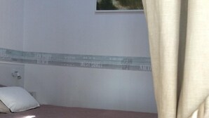 Yhden hengen sänky, jossa on tikattu peitto, tyyny ja seinälle ripustettu taulu, jossa on kuvattuna rantamaisema.