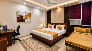 Habitación de hotel con cama, escritorio, silla, lámpara, un cuadro y unidad de aire acondicionado.