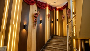 Una escalera con paneles de madera y cortinas rojas, flanqueada por luces empotradas y adornos florales.