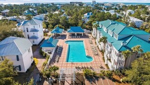 A resort with a central swimming pool, multiple buildings with blue roofs, and a surrounding landscape.