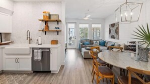 A modern kitchen with a dishwasher, a dining area with a round table and chairs, a sofa with cushions, and a ceiling fan.