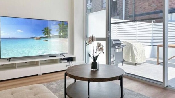 A modern living room with a flat-screen TV, a round coffee table, and a view of the sea through large windows.