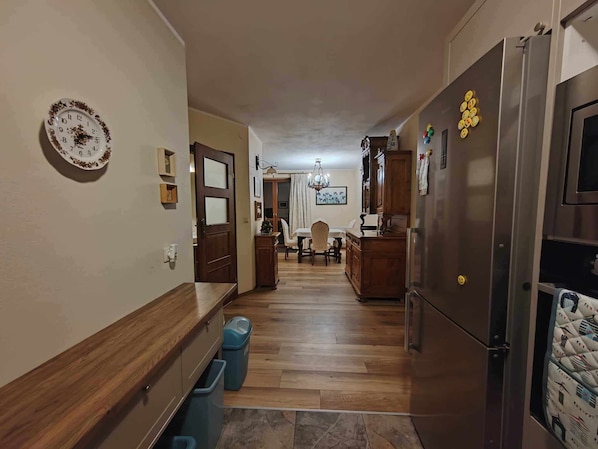 Um corredor com piso de madeira, uma área de refeições com lustre e uma cozinha com geladeira e armários.