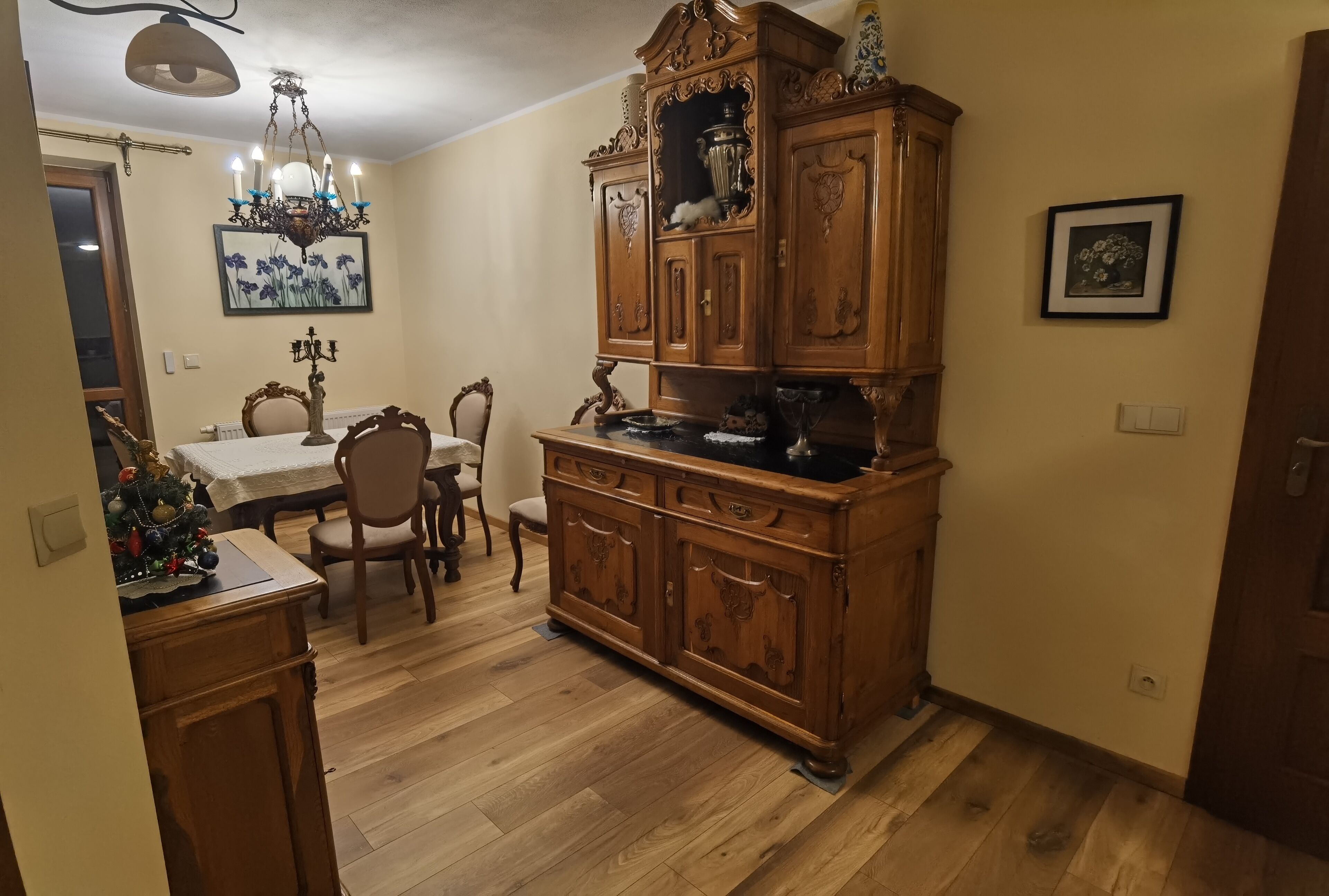 Un coin repas comprenant un buffet en bois, un lustre et une table avec des chaises.