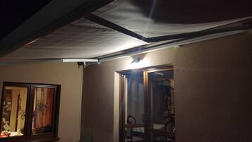 A room with a sliding glass door leading to a dining area, a window with curtains, and a ceiling with a light fixture.