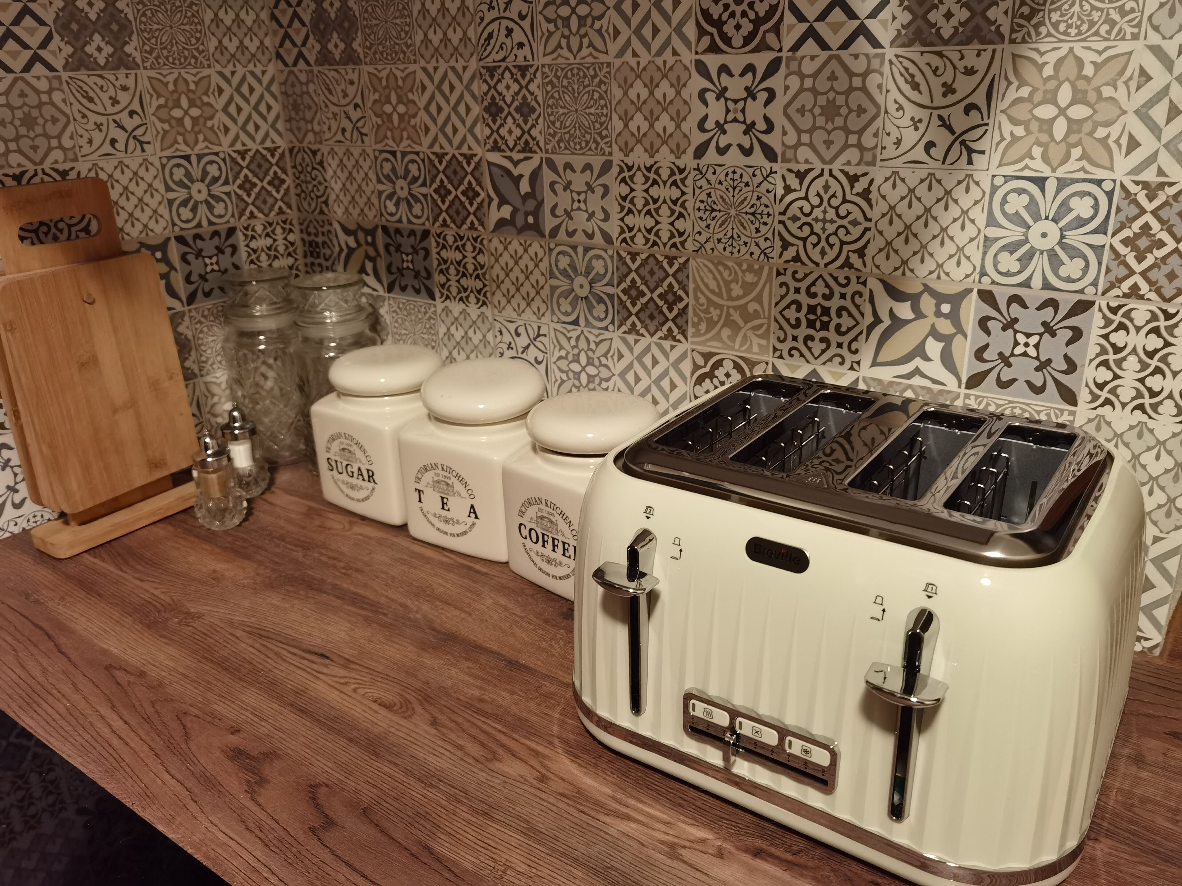 A kitchen with a vintage white toaster, sugar, tea, and coffee containers, and a wooden cutting board.