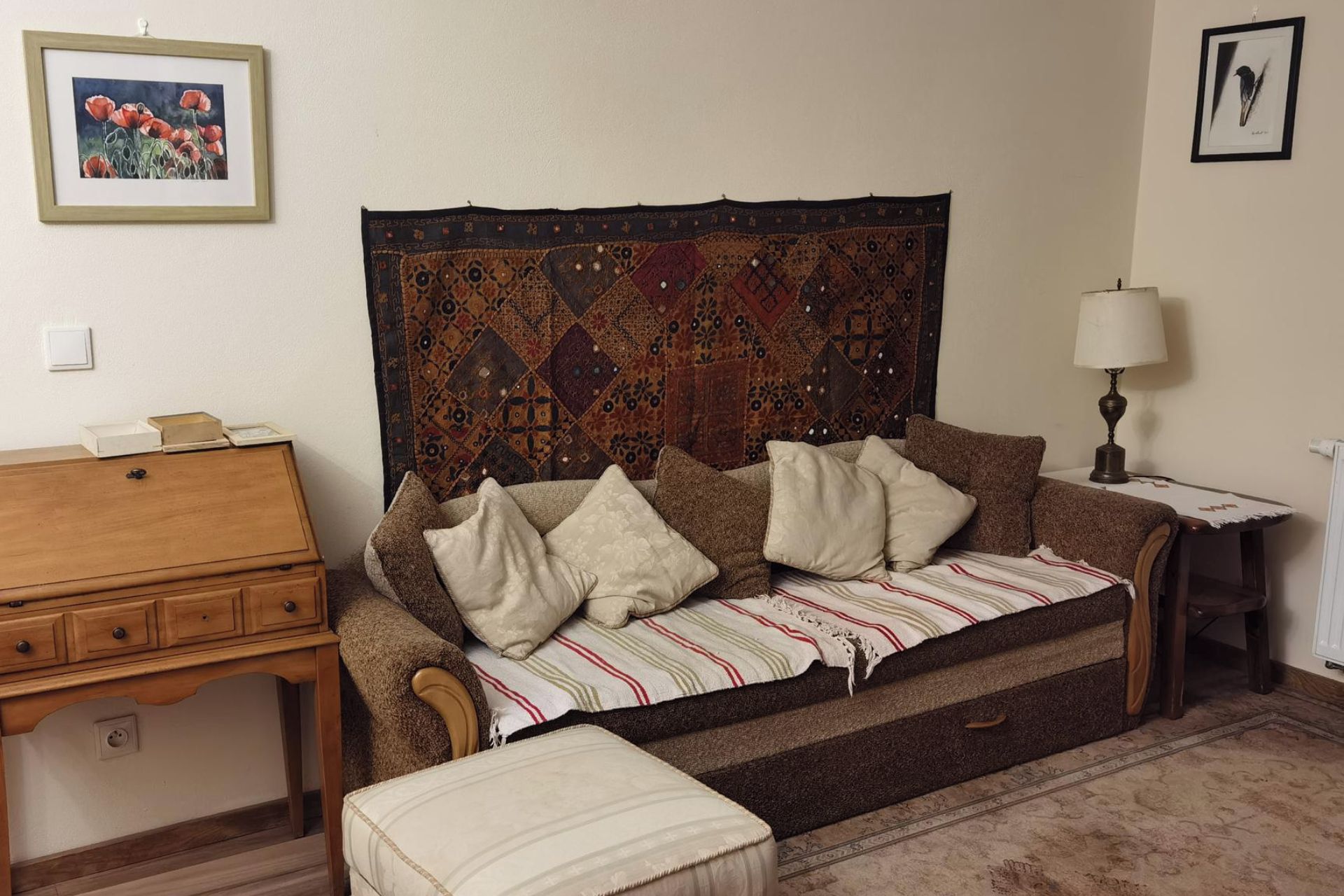Une pièce chaleureuse avec un canapé, une commode en bois, une tapisserie à motifs et un tableau encadré accroché au mur.