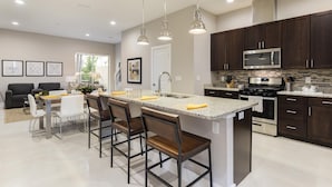 A modern kitchen with dark wood cabinets, stainless steel appliances, and a central island with bar stools. - 4 BR 4 BA Villa 5min Disney Family Getaway (Kissimmee)