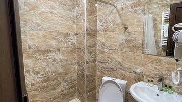 Casa de banho com chuveiro, sanita e lavatório, tudo revestido a azulejos tipo mármore.