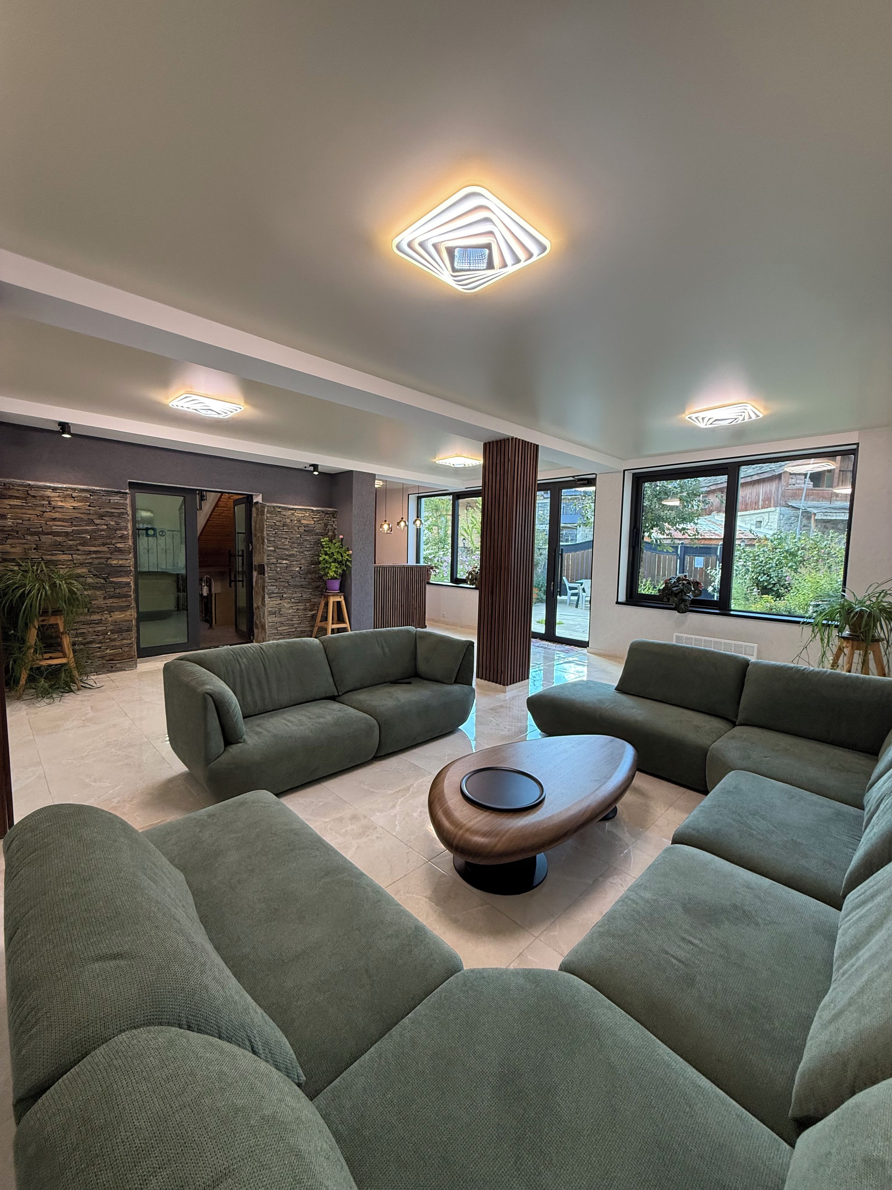 A modern living room with green sofas, a wooden coffee table, and a stone accent wall.