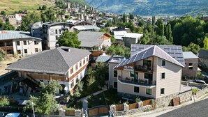 Un quartier résidentiel avec des maisons, dont un immeuble portant l’inscription « ELITE HOUSE », le tout entouré de montagnes.