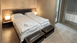 Une chambre avec deux lits, un plancher en bois, un luminaire au plafond et une fenêtre avec un rideau léger.