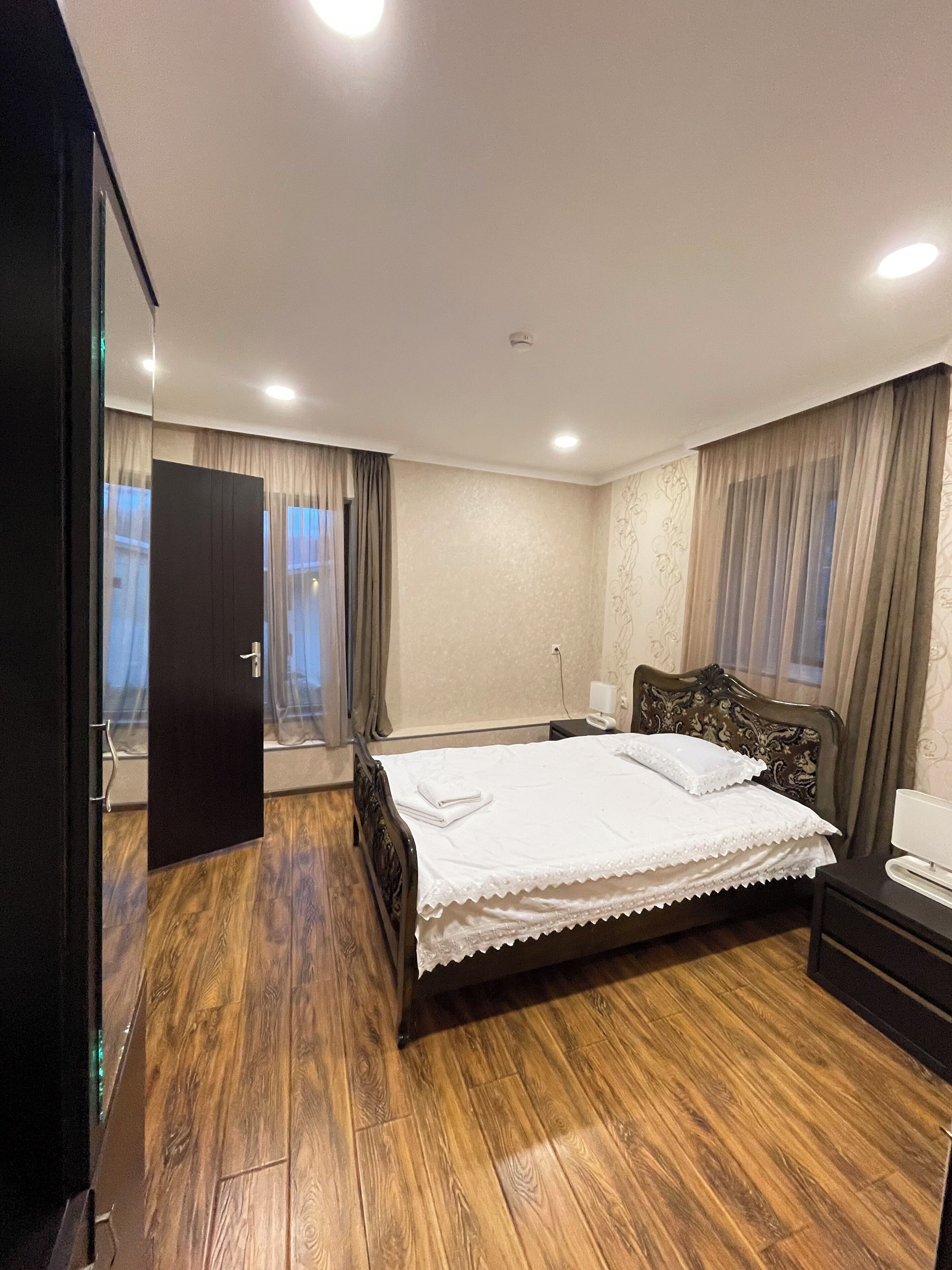 A bedroom with a wooden floor, a bed with a white bedspread, a nightstand, and a dresser.