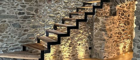 Uma escadaria de madeira com um fundo de parede de pedra, iluminada por lâmpadas penduradas.