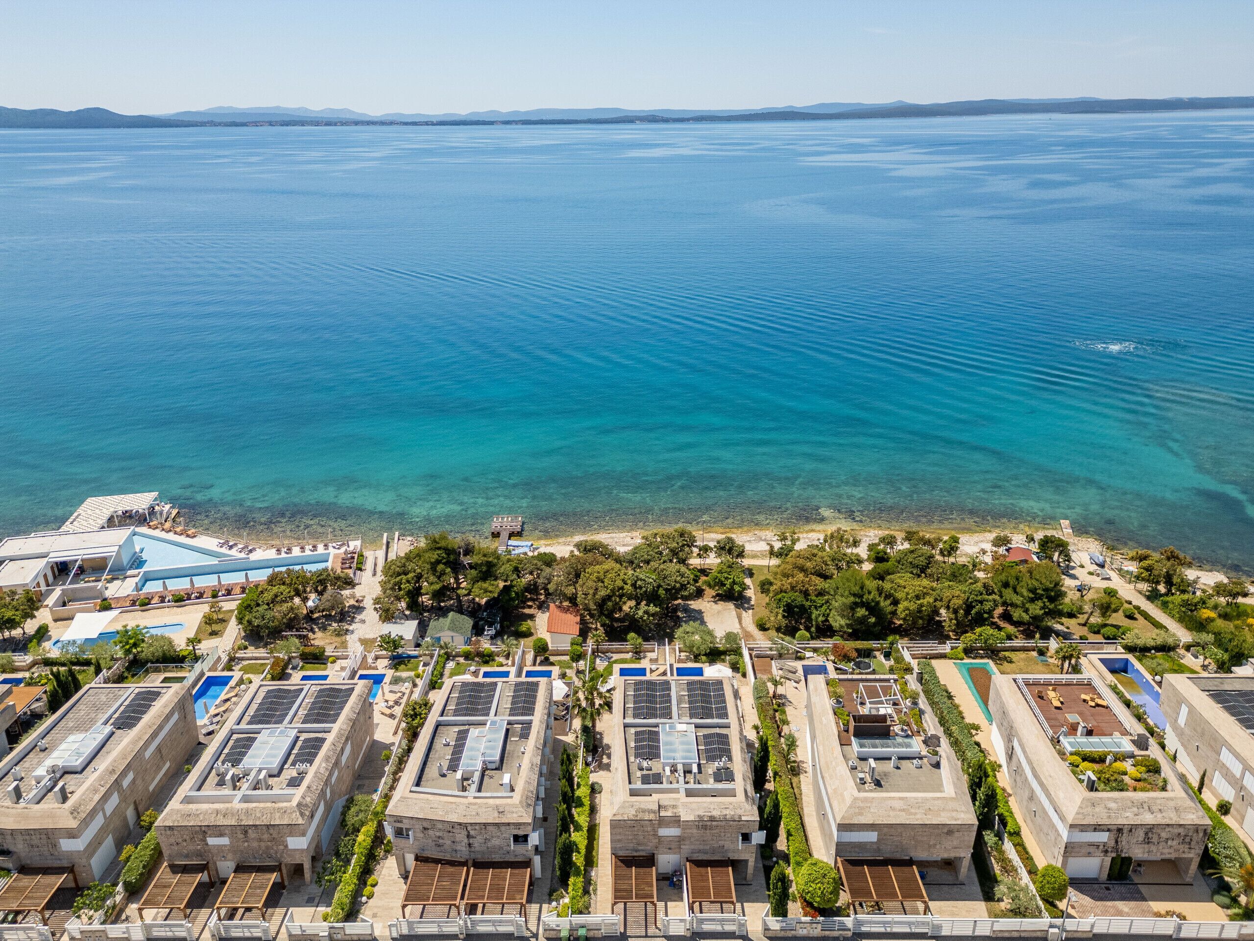A coastal hotel with multiple buildings, rooftop solar panels, and a clear view of the sea.