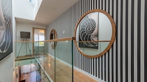 A modern interior with a glass railing, striped wall panels, and a large circular mirror. - Villa Salvia (Zadar)