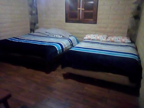 Una habitación con dos camas, suelo de madera y una ventana.