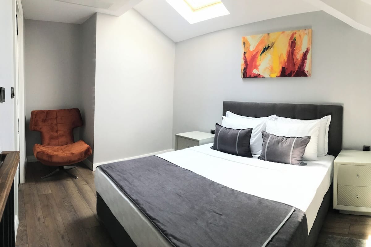 A bedroom with a bed, a nightstand, a chair, and a painting on the wall.