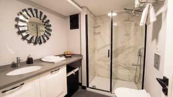 Een moderne badkamer met een ronde spiegel, een wastafel, toilet en een douche met glazen wanden.