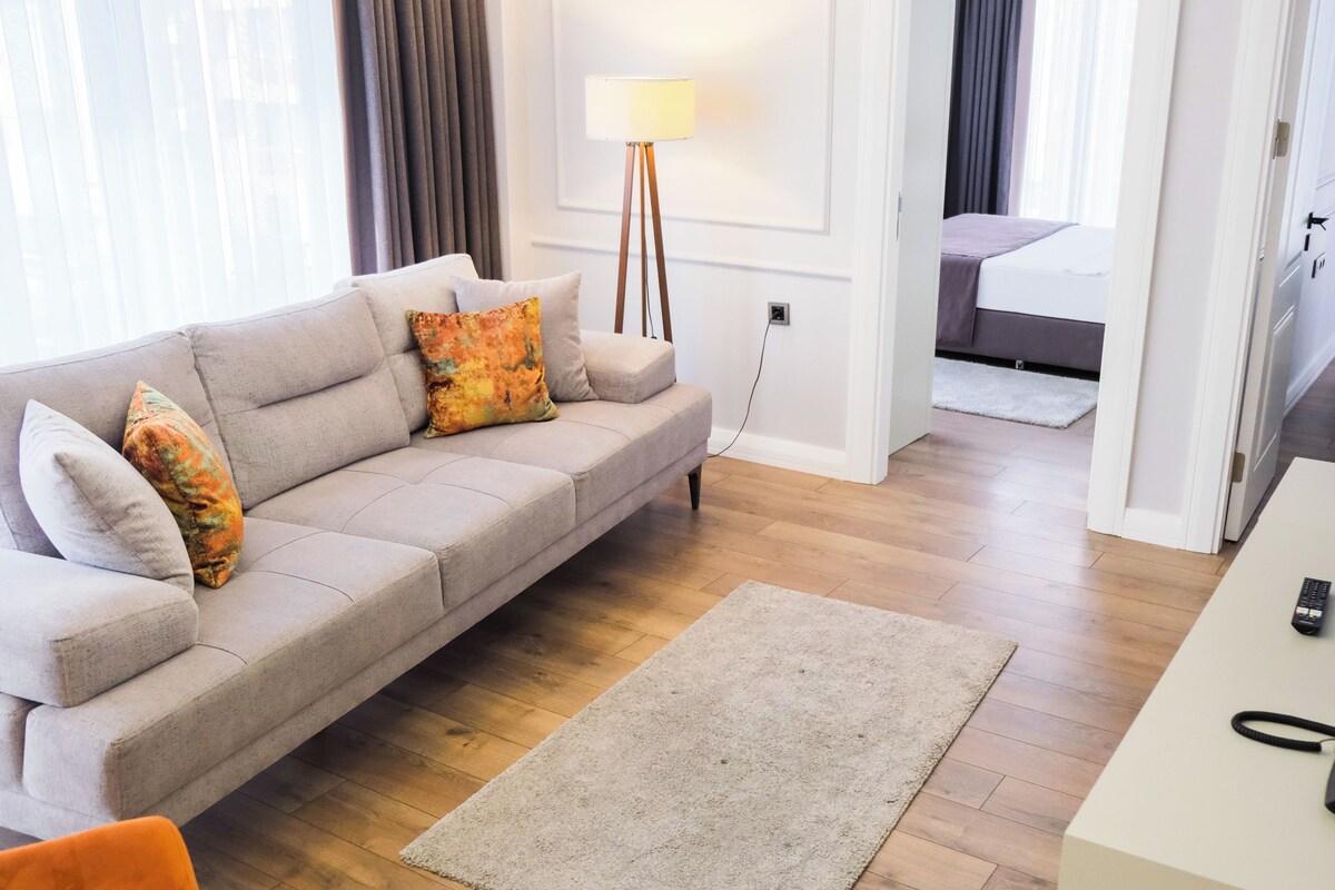 Una sala de estar moderna con un sofá, una lámpara de pie, un escritorio con un teléfono y una cama al fondo.