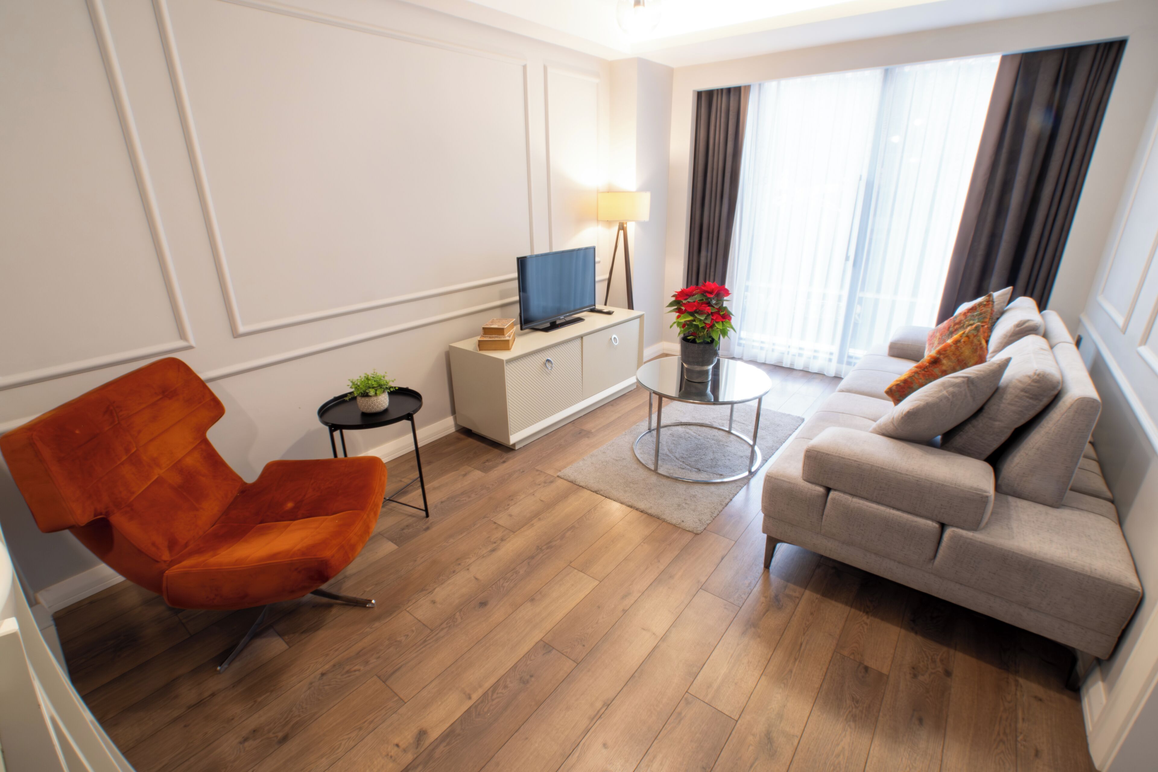 Una sala de estar moderna con un sofá, una silla, un televisor sobre un mueble, una lámpara y una planta en maceta.