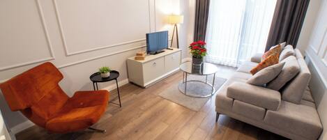 Una sala de estar moderna con un sofá, una silla, un televisor sobre un mueble, una lámpara y una planta en maceta.