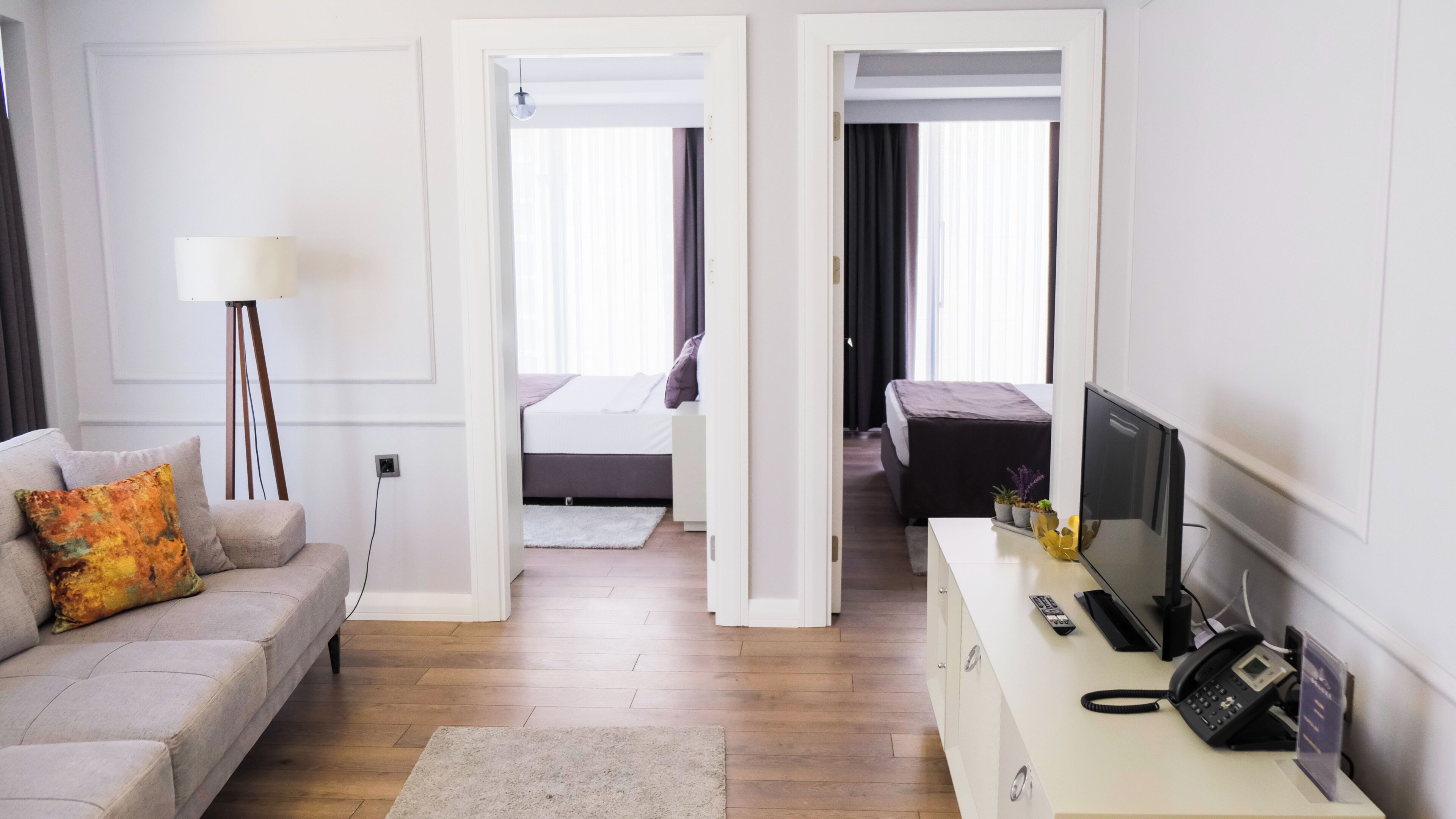 Ein Hotelzimmer mit einer Couch, einem Schreibtisch mit Telefon, einem Fernseher und einem Bett mit dunkler Bettdecke.