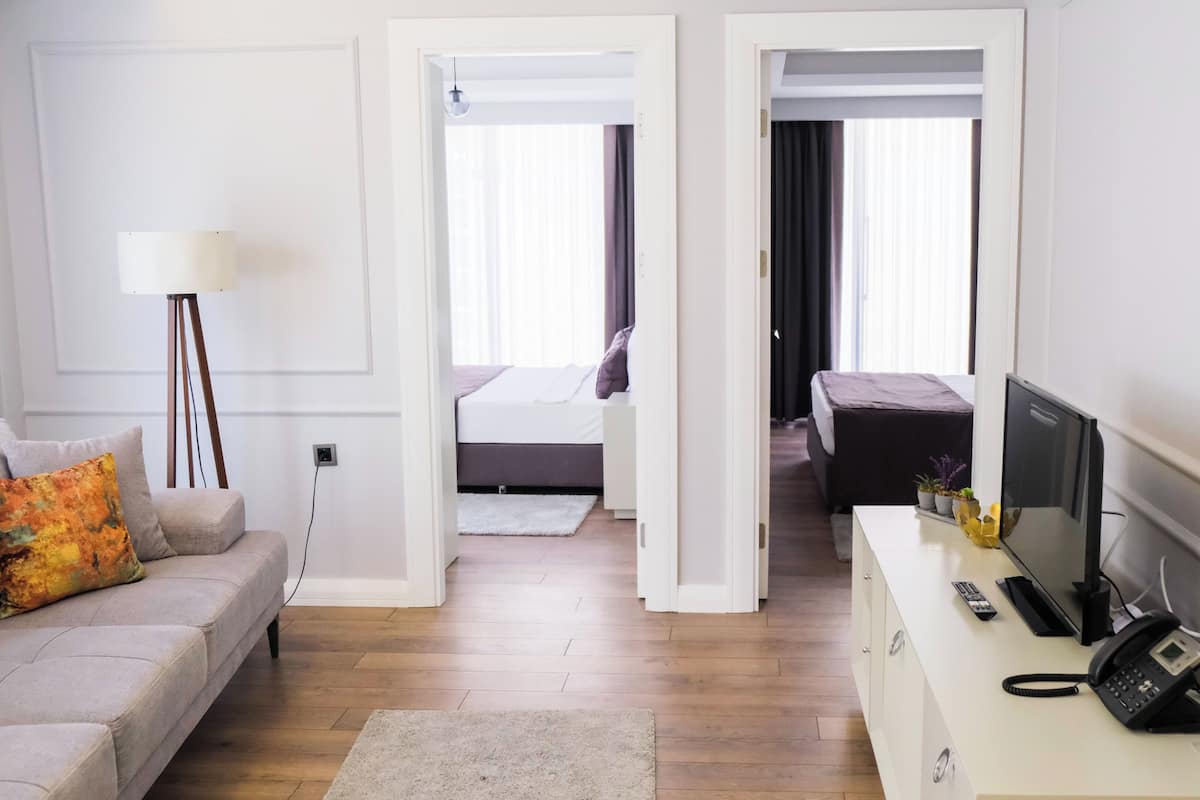 A hotel room with a sofa, a desk with a phone, a TV, and a bed with a dark bedspread.