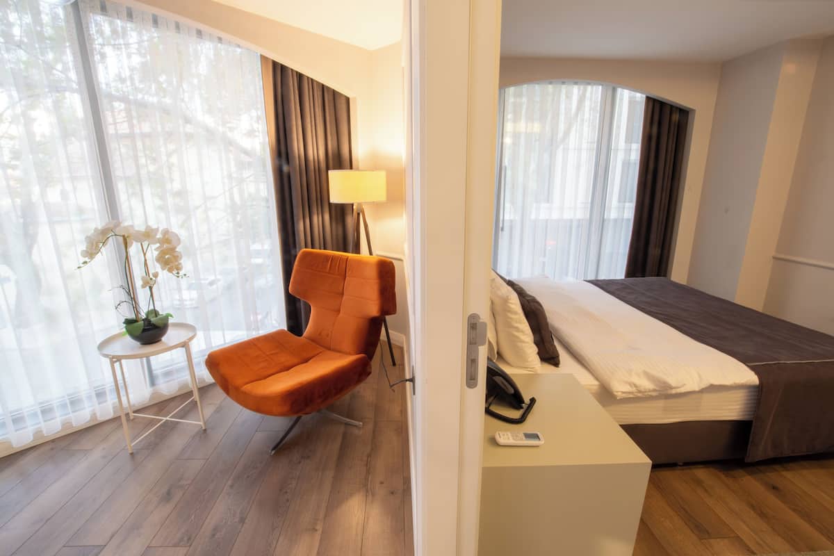 A hotel room with a bed, a chair, a small table with a plant, and a lamp.