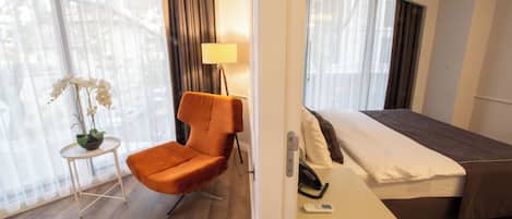 Una habitación de hotel con una cama, una silla, una mesita con una planta y una lámpara.