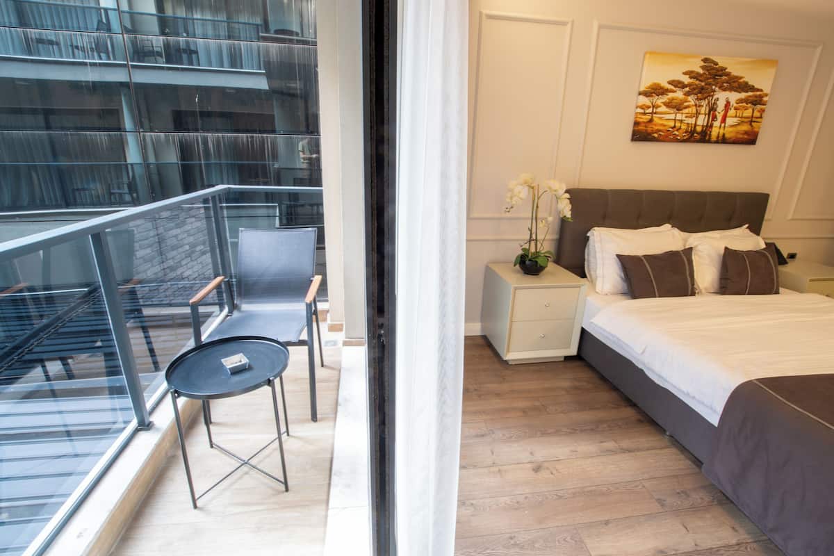 A modern hotel room with a balcony, a bed with brown bedding, a nightstand with a vase of flowers, and a painting on the wall.