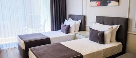 Habitación de hotel con dos camas, una mesita de noche, un cuadro en la pared y vistas al exterior a través de amplias ventanas.
