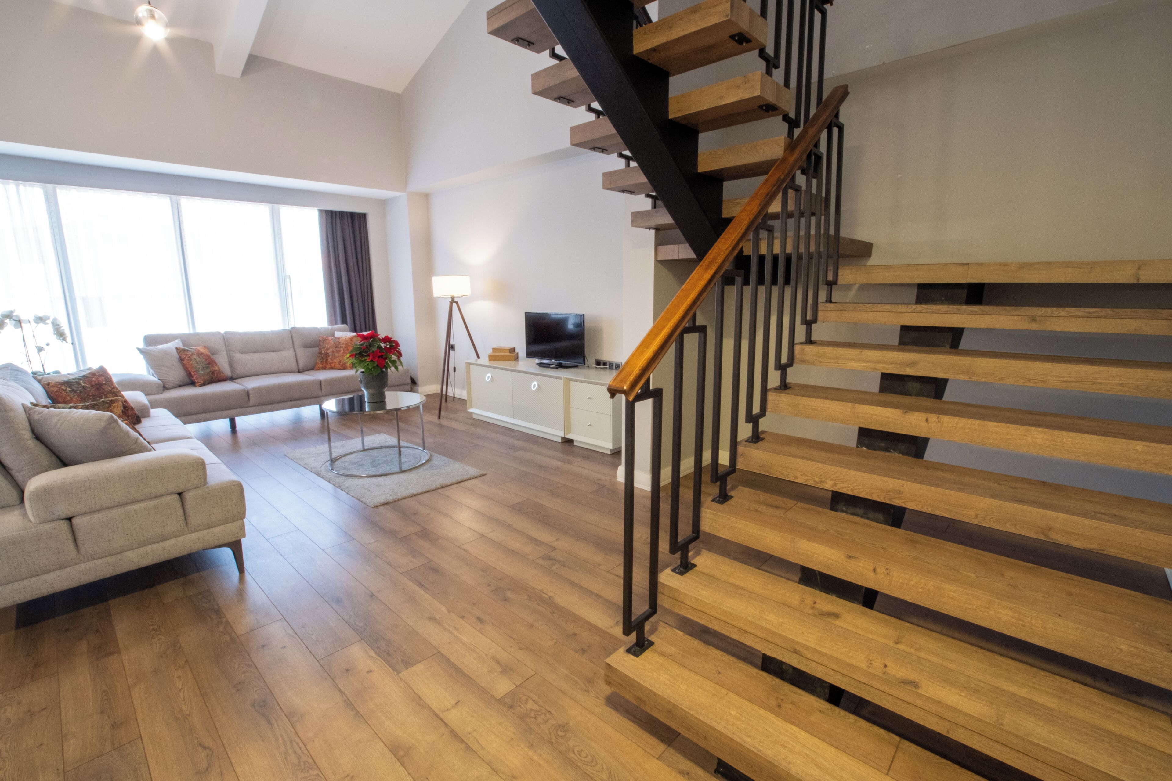 Ein modernes Wohnzimmer mit Holzboden, einer Treppe, einem Sofa, einem Couchtisch und einem Fernseher.