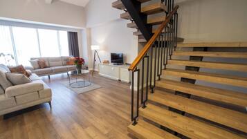 A modern living room with a wooden staircase, a sofa, a coffee table, and a TV.