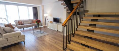 A modern living room with a wooden staircase, a sofa, a coffee table, and a TV.