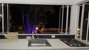 A kitchen with a sink, stove, and a window overlooking a balcony with palm trees and lights. - Hermosa Casa Campestre a 1 Hora de Bogotá - Tena (TENA)