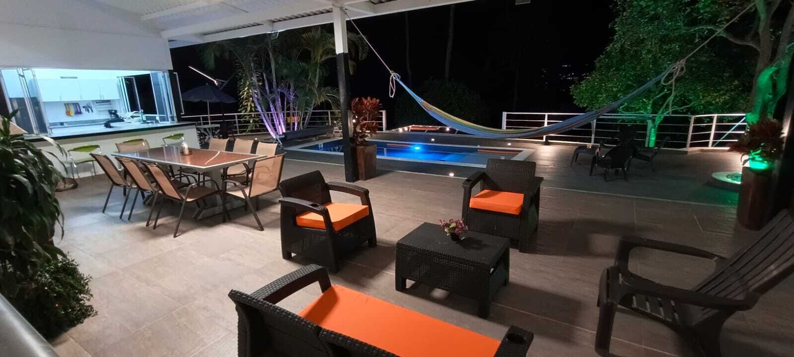 Et overdækket udendørs område med pool, spisebord, stole og loungesæde.