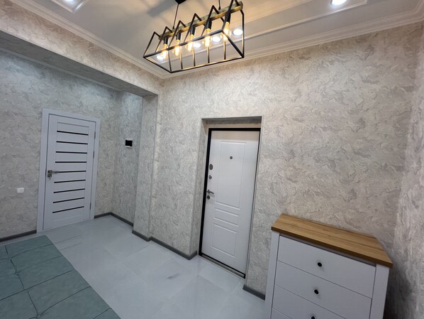 A hallway with a patterned wall, a white door, a white cabinet, and a green rug.