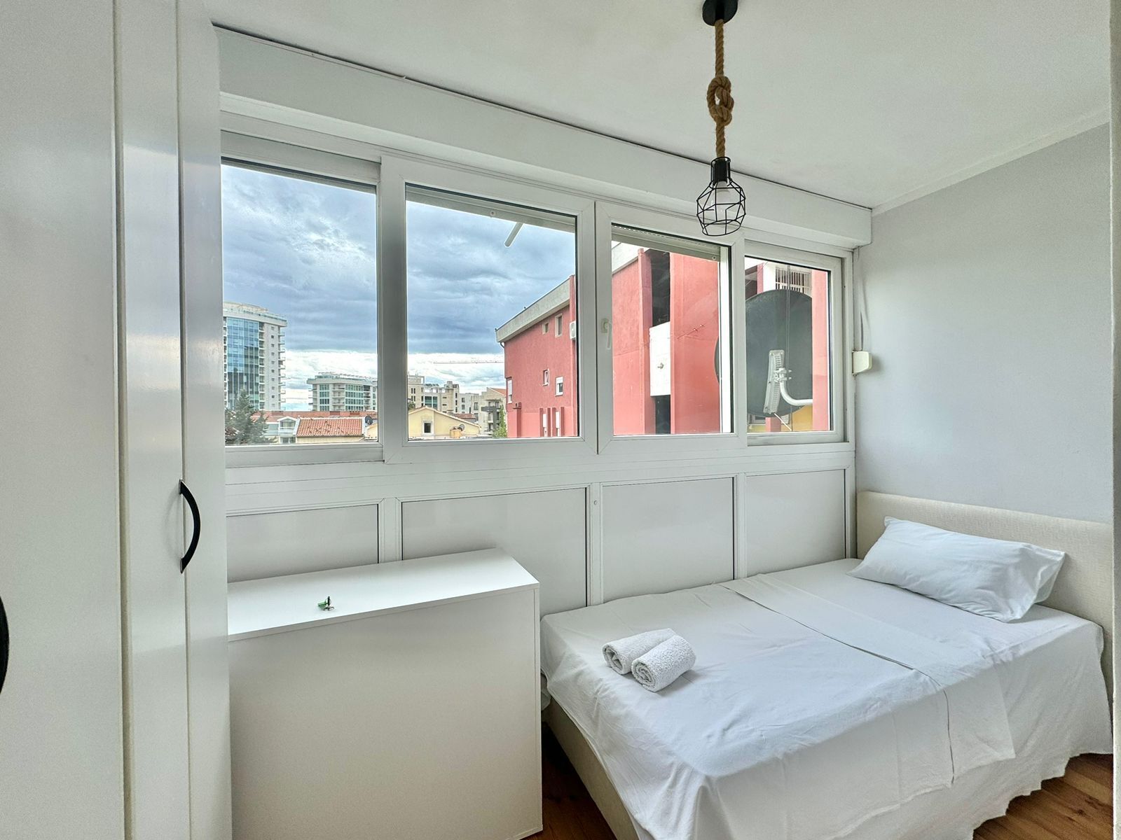 Un dormitorio con cama, ventana y vistas a edificios.