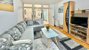 Un salon moderne avec un canapé gris à motifs, une table basse en verre et un meuble TV en bois.