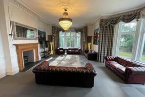 A spacious living room with a large dark sofa, a smaller sofa, and a fireplace. - 22 Bedroom Huge Holiday Home in fabulous location (Bontnewydd)