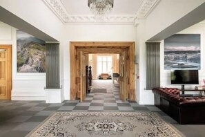 A spacious hallway with a checkered floor, a wooden door, and a view into a room with a sofa and a television. - 22 Bedroom Huge Holiday Home in fabulous location (Bontnewydd)