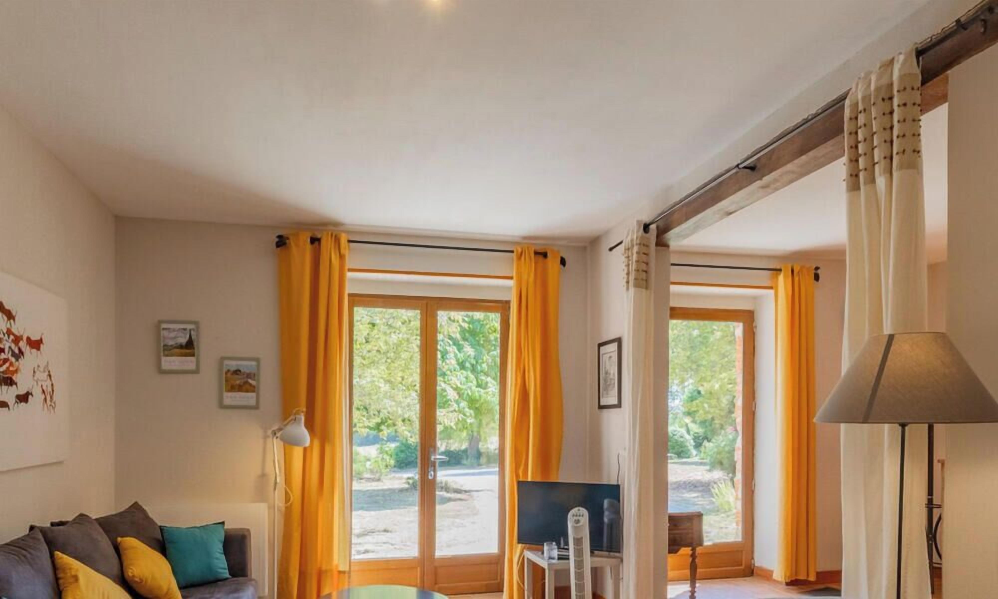 Une pièce avec un canapé, une télévision et une table. Il y a des rideaux aux fenêtres.
