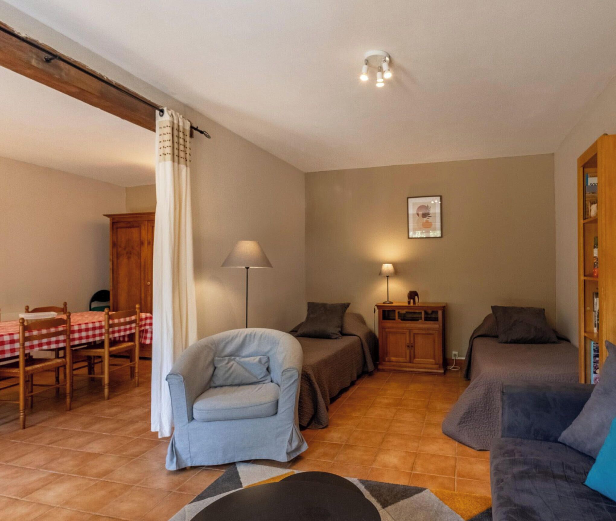 Ein Wohnzimmer mit einer Couch, einem Sessel, einem Tisch mit kariertem Tischläufer, einer Lampe und einem Schrank.