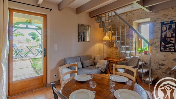 Un comedor con una mesa de madera dispuesta para cuatro personas, rodeada de sillas. Una escalera con barandilla de metal conduce a un nivel superior.