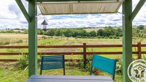 Un espacio de estar techado al aire libre con vistas a un paisaje rural, incluyendo campos y una construcción distante.